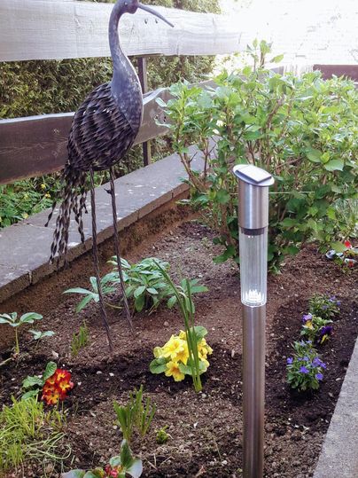 Een mooie tuin met kleurrijke bloemen en een decoratieve vogel van metaal. Op de achtergrond staat een apparaat voor de bodemvochtigheid.