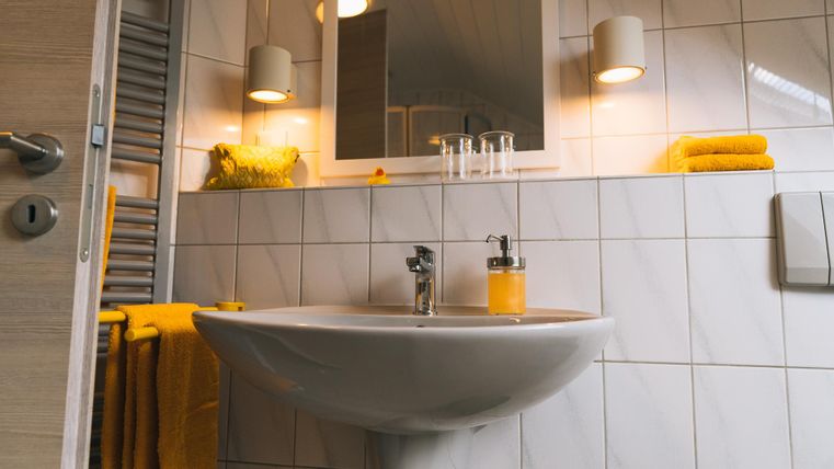 Een moderne badkamer met een witte wastafel en een grote spiegel. Gele handdoeken en decoratieve elementen zorgen voor een gezellige sfeer.