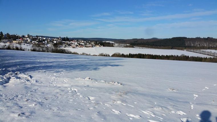 Eine schneebedeckte Landschaft mit einem Blick auf ein Dorf am See. Der Himmel ist klar und blau.