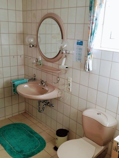 Een schone badkamer met een toilet en een wasbak. Op de grond liggen groene badmatten.