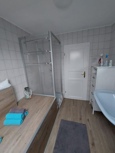 A modern bathroom with a shower cubicle and a bathtub. The walls are tiled in light colors, and fresh towels are neatly arranged.
