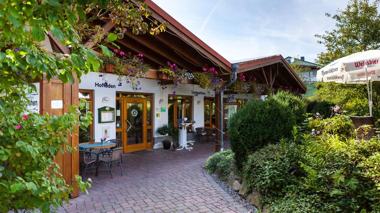 An inviting restaurant with a lovely entrance and blooming plants. The paved path leads to the door, surrounded by green vegetation.