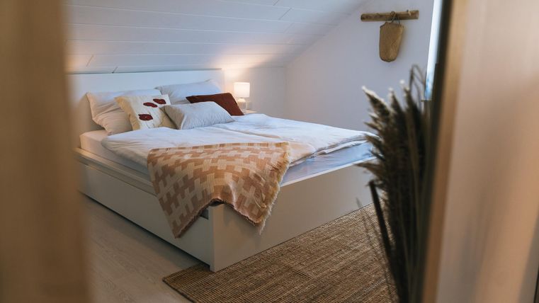 Een gezellige slaapkamer met een groot bed en zachte kussens. De ruimte heeft warm licht en een natuurlijk, uitnodigend tapijt.