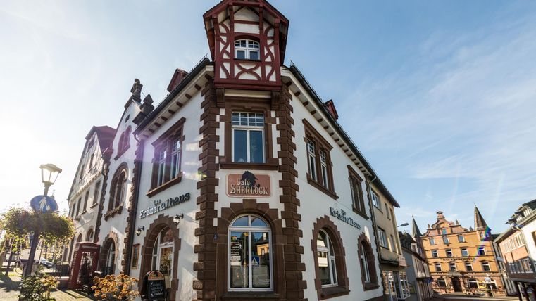 Historic building with Café Sherlock and Crime House at a street corner, blue sky in the background.