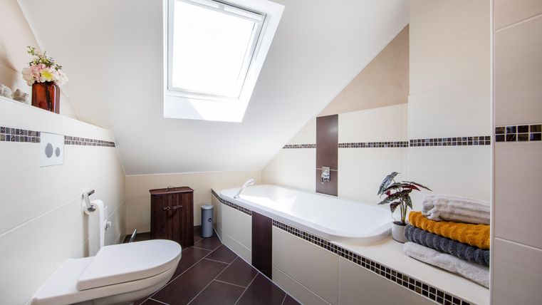Ein modernes Badezimmer mit einer Badewanne und einer Toilette. Das Licht fällt durch ein Dachfenster auf die stilvolle Einrichtung.