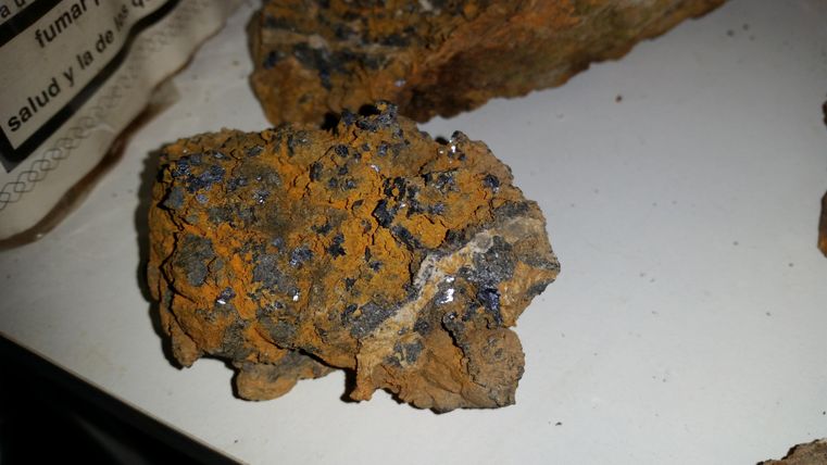 Een stuk gesteente met een oranje oppervlak en kleine glinsterende mineralen. De structuur is ruw en onregelmatig.