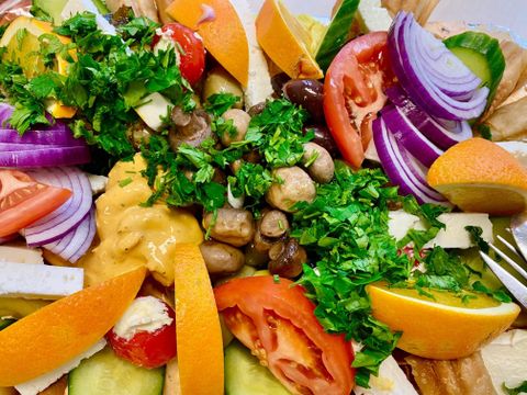 Ein bunter Salat mit frischem Gemüse, darunter Tomaten, Gurken und Zwiebeln. Das Gericht ist mit Kräutern und einem cremigen Dressing garniert.