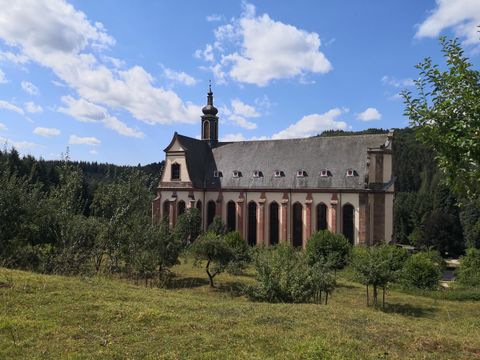 Eine alte Kirche umgeben von grünen Wiesen und Bäumen. Der Himmel ist blau mit einigen weißen Wolken.
