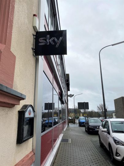 Een gebouw met een zwart sky-schild. De straat is omzoomd met verschillende auto's en verkeersborden.