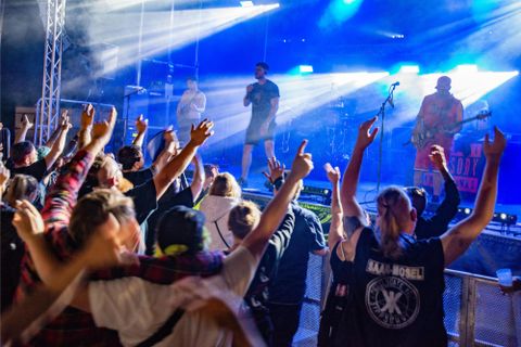 Eine große Menschenmenge jubelt bei einem Live-Konzert. Die Bühne ist beleuchtet, und die Künstler performen mit Energie.