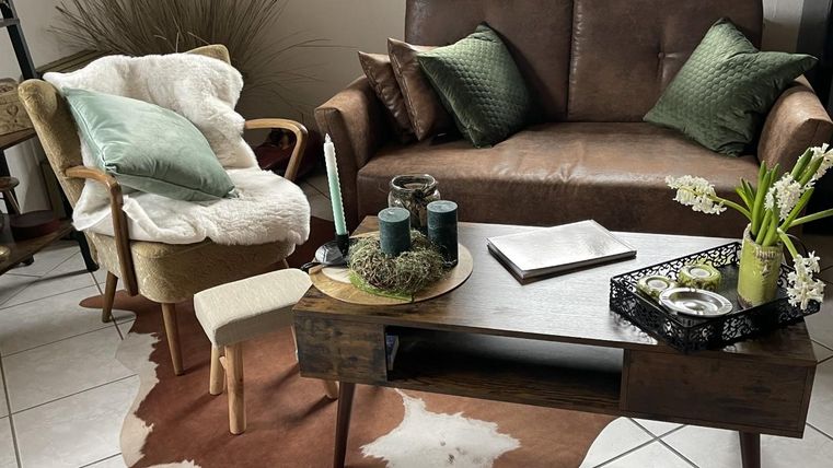 Een gezellige woonkamer met een bruine leren bank en een comfortabele stoel. Op de tafel staan decoraties en een klein plantje.