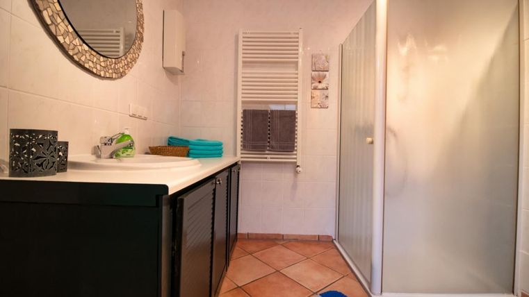 A modern bathroom with a shower cabin and a large mirror. The floor is tiled and there are colored towels.