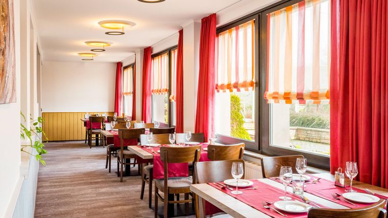 An inviting restaurant with wooden chairs and red-and-white striped curtains. The tables are elegantly set and offer a view outside.