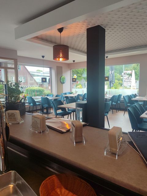 A modern restaurant with cozy tables and chairs. The large window front offers a view of the outdoor area.