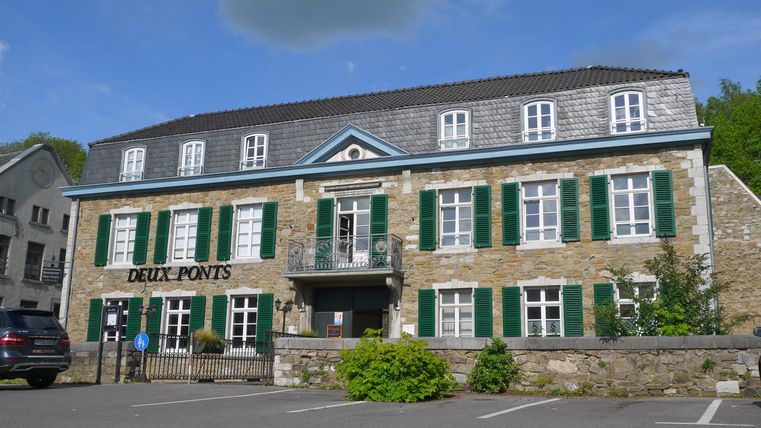 Een charmant stenen gebouw met groene luiken in een rustige omgeving. Het gebouw herbergt een restaurant genaamd "Deux Ponts".