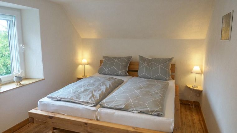Ein gemütliches Schlafzimmer mit einem Doppelbett und modernen Bettdecken. Das Zimmer hat eine helle Atmosphäre mit einer großen Fensterfront und warmem Holzfußboden.