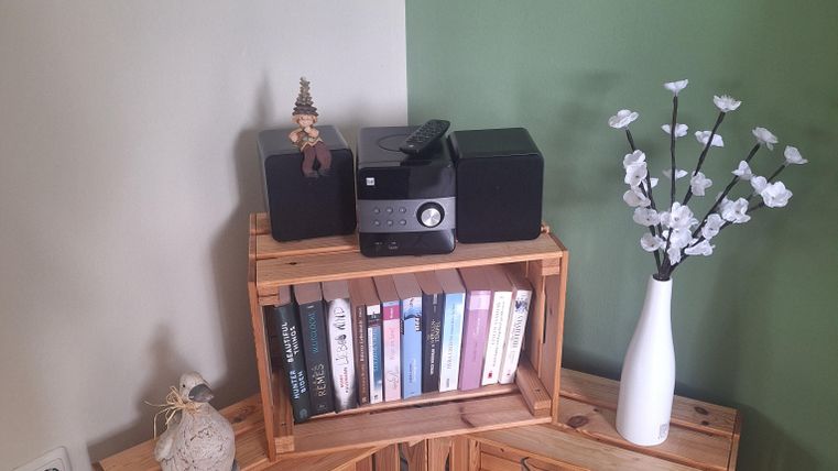 Ein stilvolles Arrangement aus Holzkisten, die Bücher und Dekorationsobjekte halten. Auf der Oberseite stehen ein Lautsprecher und eine Vase mit Blumen.