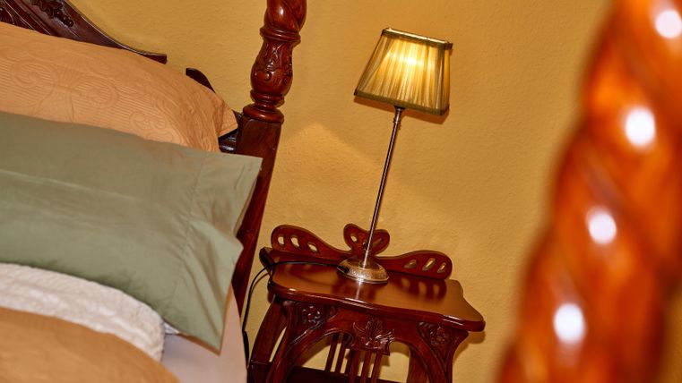 A cozy bedroom with a large bed and elegant bedding. Next to the bed is a wooden nightstand with a small lamp.