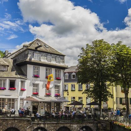 Ein charmantes Café mit Restaurant und Hotel in einer malerischen Stadt. Blühende Blumen und gemütliche Terrassen laden zum Verweilen ein.