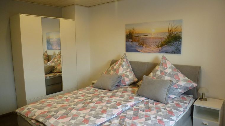 Ein gemütliches Schlafzimmer mit einem großen Doppelbett und bunten Kissen. An der Wand hängt ein Bild einer Landschaft, und ein Kleiderschrank steht daneben.