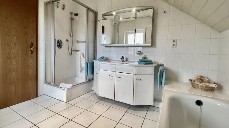 Ein modernes Badezimmer mit einer Dusche, einem Spiegel und einem Waschbecken. Die Wände sind gefliest und das Licht sorgt für eine helle Atmosphäre.