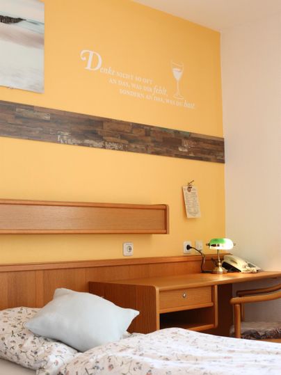 Ein gemütliches Schlafzimmer mit einem Holzbett und einer gelben Wand. Auf dem Nachtisch steht eine Lampe und ein Telefon.