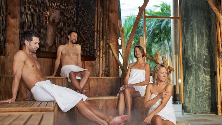 Een groep van vier personen ontspant in een sauna. Ze dragen handdoeken en genieten van de rustige sfeer.