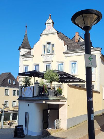 Een charmant gebouw met een neogotische toren en een balkon. Op de voorgrond staat een straatlantaarn.