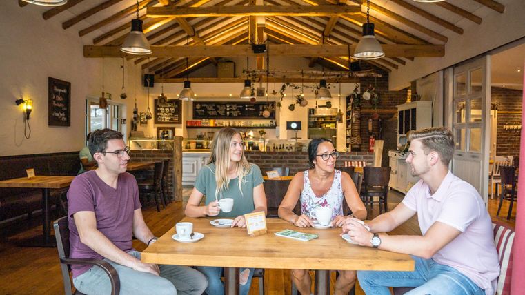 Een groep van vier vrienden zit aan een houten tafel in een gezellig café. Ze lachen en genieten van hun drankjes in een uitnodigende sfeer.