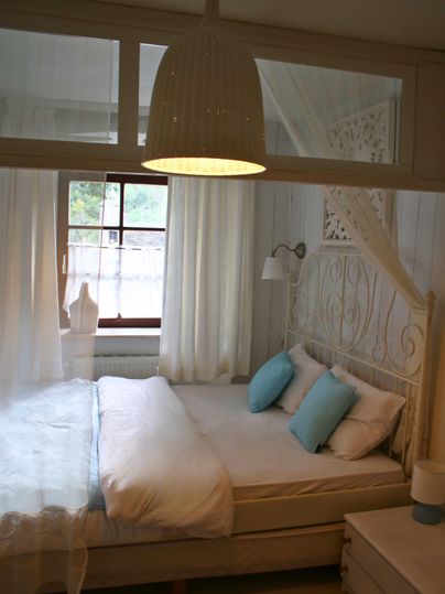 A cozy bedroom with a large bed and light curtains. The decor is simple and modern, featuring a beautiful pendant light and decor in soft colors.