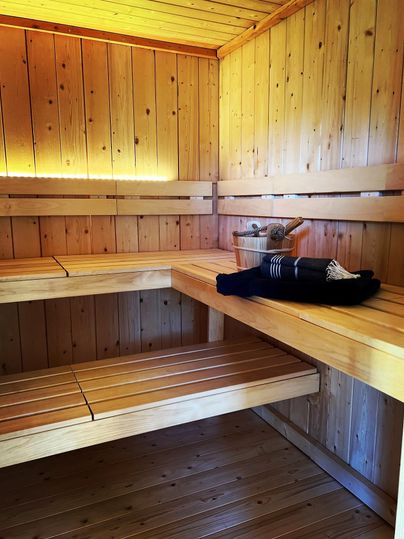 Eine gemütliche Sauna mit holzverkleideten Wänden und Bänken. Ein Handtuch und ein Eimer stehen auf der oberen Ablage.