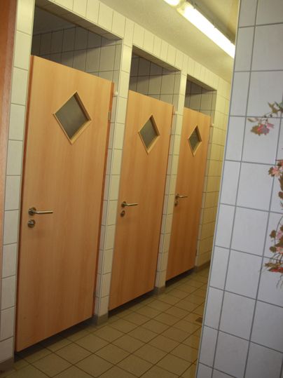 Drei Holz-Türen mit rechteckigen Fenstern in einem Badezimmer. Der Boden ist gefliest und die Wände sind hell gefliest.