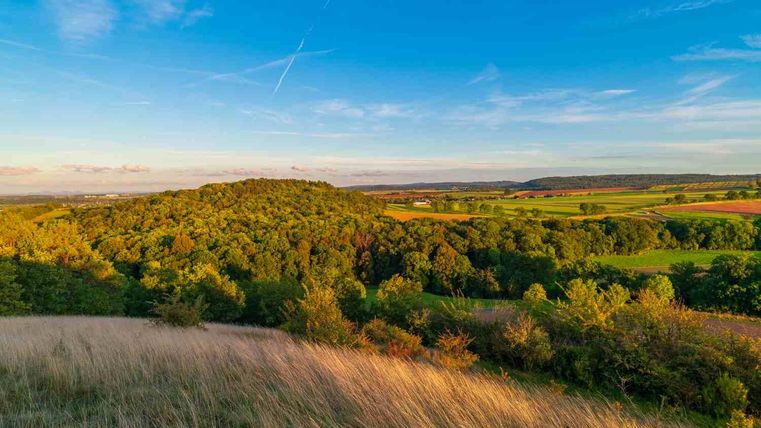 Een schilderachtig landschap met zachte heuvels en weelderig groen. De lucht is helder en stralend blauw.