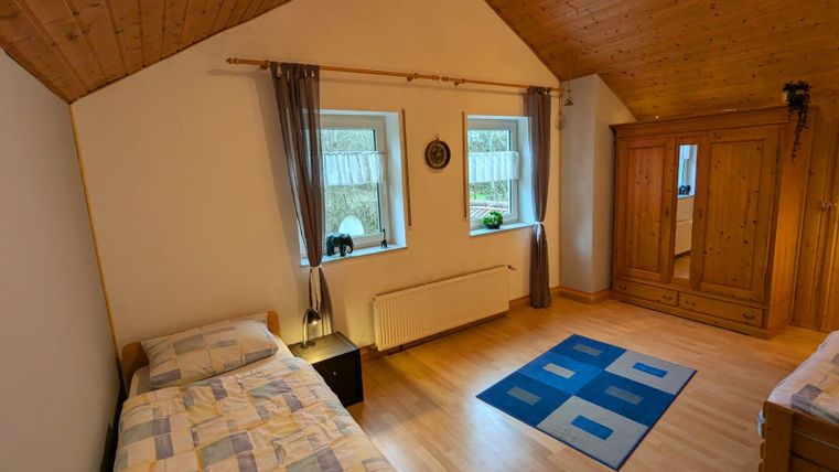 A cozy bedroom with two single beds and wooden walls. The windows provide plenty of natural light and the carpet gives the room a warm atmosphere.