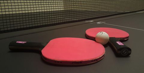 Two table tennis rackets with red hitting surfaces and a ball lie on a dark table tennis table.