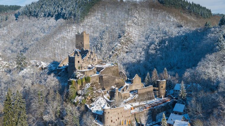 Eine alte Burg liegt in einer schneebedeckten Landschaft, umgeben von Wald. Die klare Winterluft und der Schnee verleihen der Szene eine magische Atmosphäre.