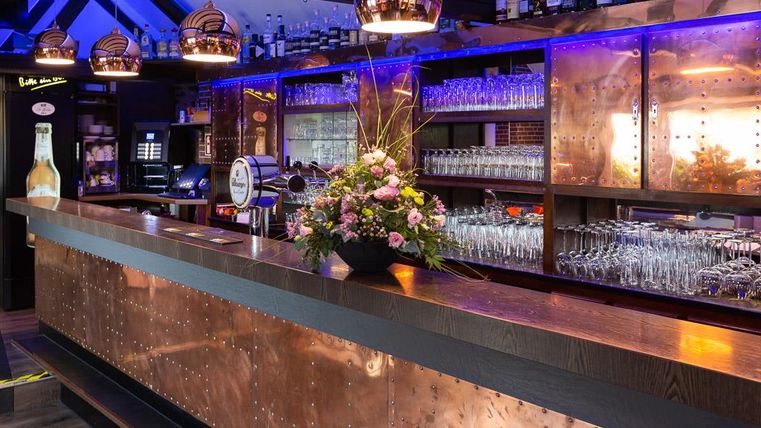 A stylish bar with a shiny copper surface and elegant lighting. Floral arrangements and glasses add an inviting touch to the atmosphere.