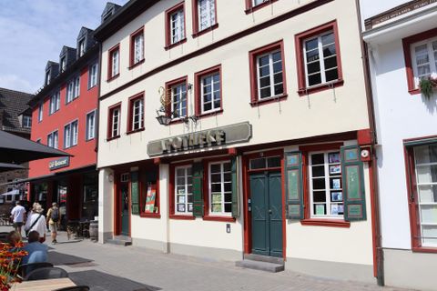 Een historisch gebouw met het opschrift "Apotheek". De gevel is licht geverfd en heeft veel ramen met bloembakken.