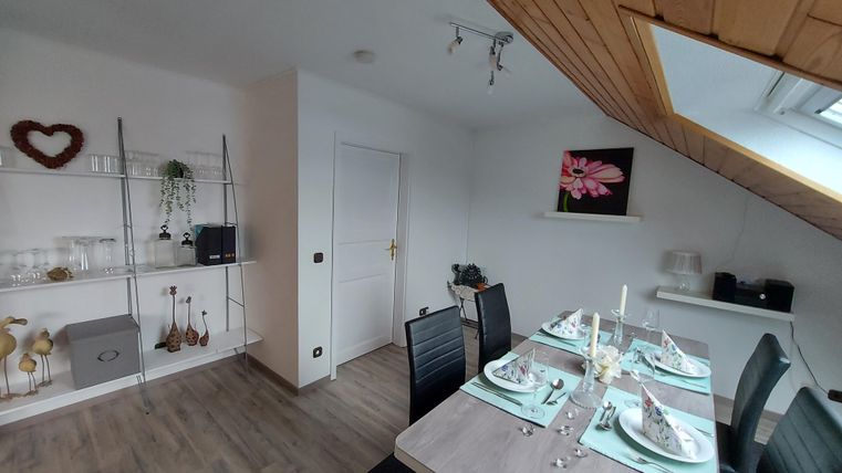 A cozy dining area with a modern table and chairs. A picture of a flower hangs on the wall, and the room is bright and friendly decorated.