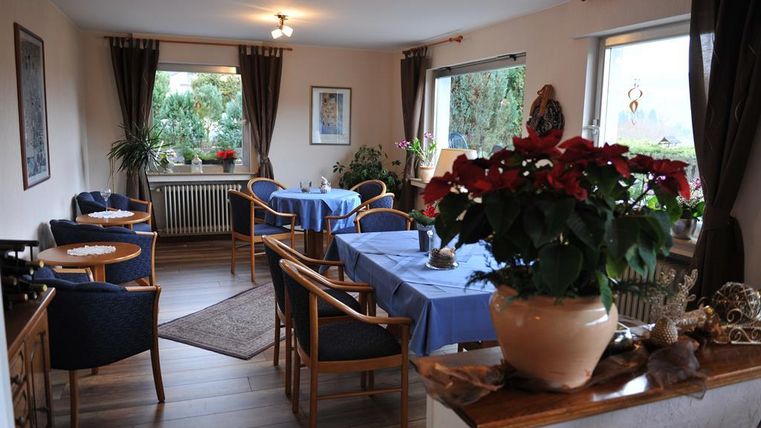 A cozy room with blue tablecloths and wooden chairs. Plants and decorations give the atmosphere an inviting character.