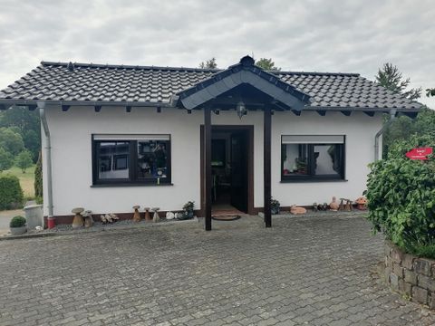 Een gezellig huis met een zwart dak en witte muren. De ingang is omgeven door een bestraat oppervlak.