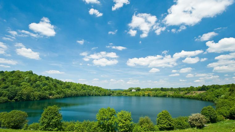 A beautiful lake surrounded by green hills and trees. The sky is clear and blue with some clouds.