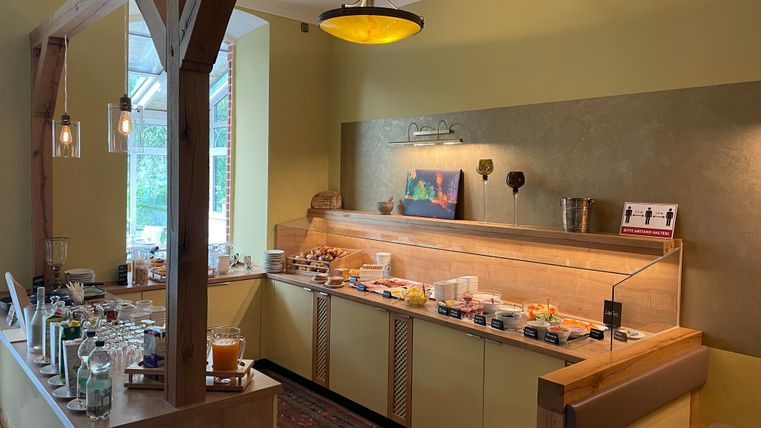 Ein Frühstücksbuffet in einem gemütlichen Raum. Es gibt eine Auswahl an Speisen und Getränken, schön präsentiert auf einem langen Tisch.