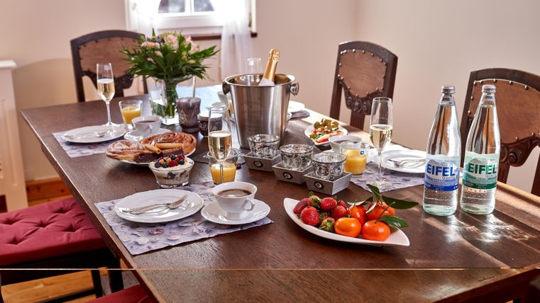 A beautifully set table with glassware, fruit, and snacks. In the background, there is a bottle of sparkling wine and mineral water.