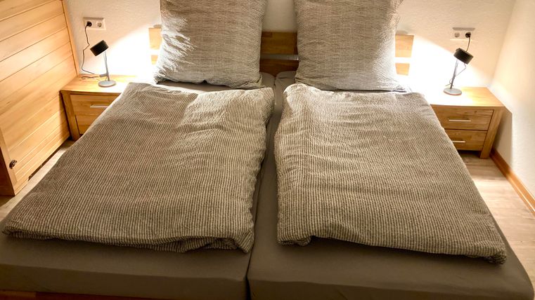 Ein gemütliches Schlafzimmer mit einem Doppelbett und zwei großen Kissen. Neben dem Bett stehen zwei Nachttische mit modernen Lampen.