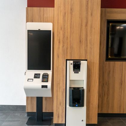 Ein neuer Automat für Bestellungen steht neben einem Getränkeautomaten. Die Wände sind mit Holzpaneelen und rotem Akzent gestaltet.