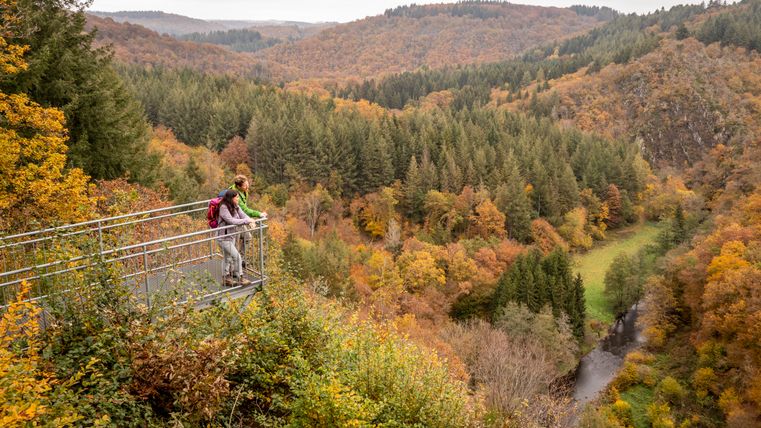 Zwei Personen auf einer Aussichtsplattform mit Blick auf ein herbstliches Tal.