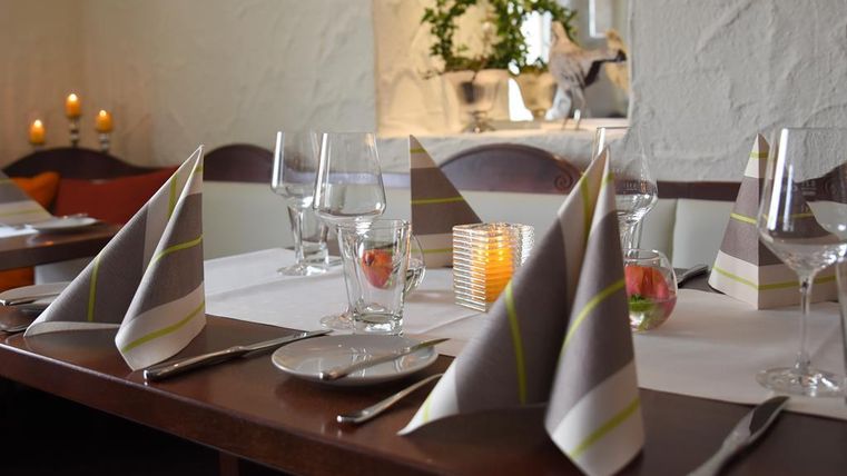 Ein elegant gedeckter Tisch in einem Restaurant. Die Dekoration umfasst gefaltete Servietten, Gläser und Kerzenlicht.