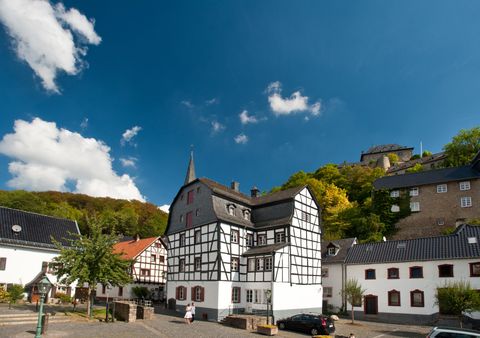 Ein malerisches Dorf mit Fachwerkhäusern und grünen Hügeln im Hintergrund. Der Himmel ist klar und blau, ideal für einen entspannten Tag.