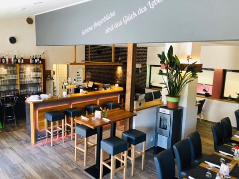 Modern restaurant with bar, wooden tables and chairs. On the wall, it says "Beautiful moments are the happiness of life." Plants and glasses decorate the room.